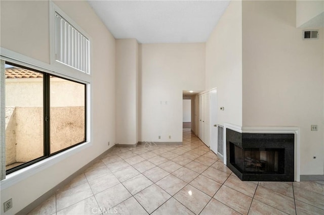 unfurnished living room with visible vents, baseboards, a high ceiling, a multi sided fireplace, and light tile patterned floors