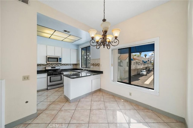 kitchen with dark countertops, appliances with stainless steel finishes, a peninsula, a chandelier, and white cabinetry