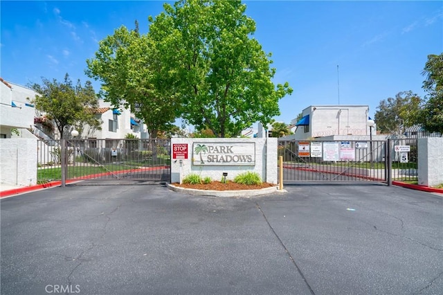 community sign with a residential view, fence, uncovered parking, and a gate