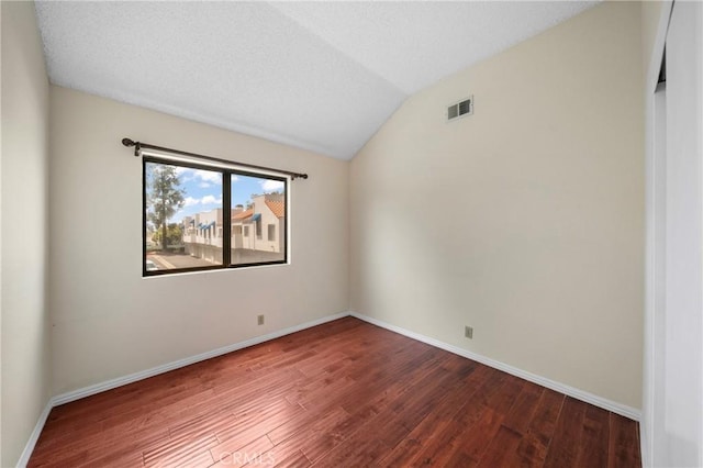 spare room with baseboards, lofted ceiling, wood finished floors, and visible vents