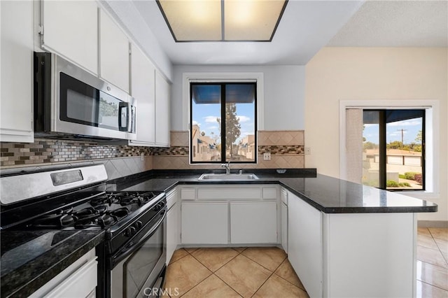 kitchen featuring dark countertops, a sink, stainless steel appliances, a peninsula, and light tile patterned floors