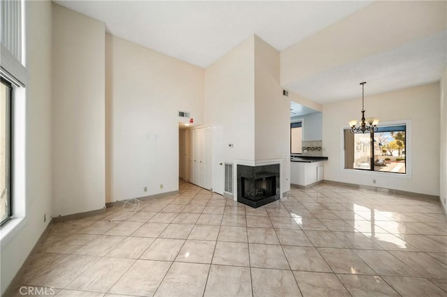 unfurnished living room with a chandelier, a multi sided fireplace, baseboards, a towering ceiling, and visible vents