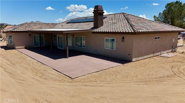 back of property featuring a tiled roof, a patio, a chimney, and stucco siding