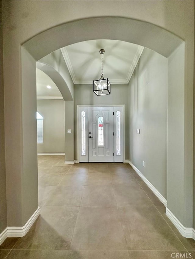 entrance foyer with crown molding, an inviting chandelier, arched walkways, tile patterned floors, and baseboards