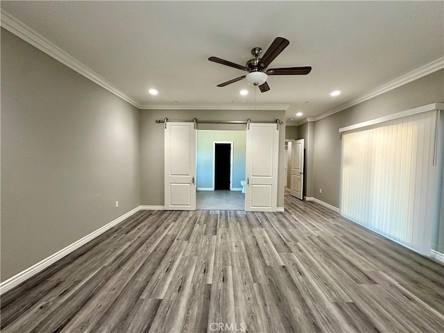 unfurnished bedroom featuring a barn door, recessed lighting, baseboards, wood finished floors, and ornamental molding
