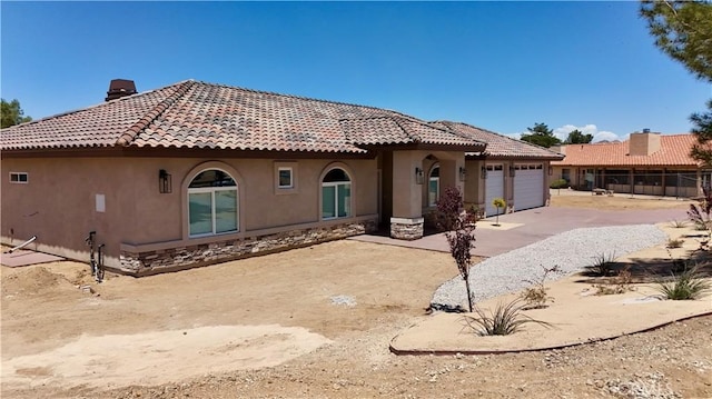 back of property with a garage, stucco siding, a chimney, driveway, and a tile roof