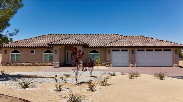 mediterranean / spanish home with a garage, stucco siding, a tiled roof, and concrete driveway