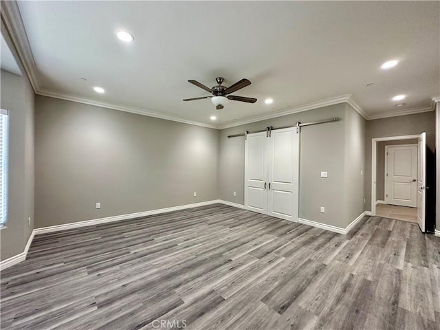 unfurnished bedroom with recessed lighting, baseboards, a barn door, and wood finished floors