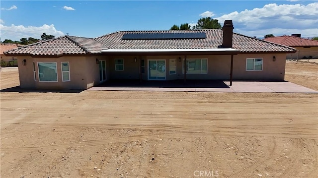 back of property featuring roof mounted solar panels, stucco siding, a tiled roof, and a chimney