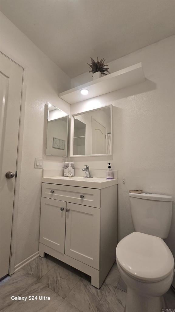 bathroom featuring vanity, marble finish floor, baseboards, and toilet