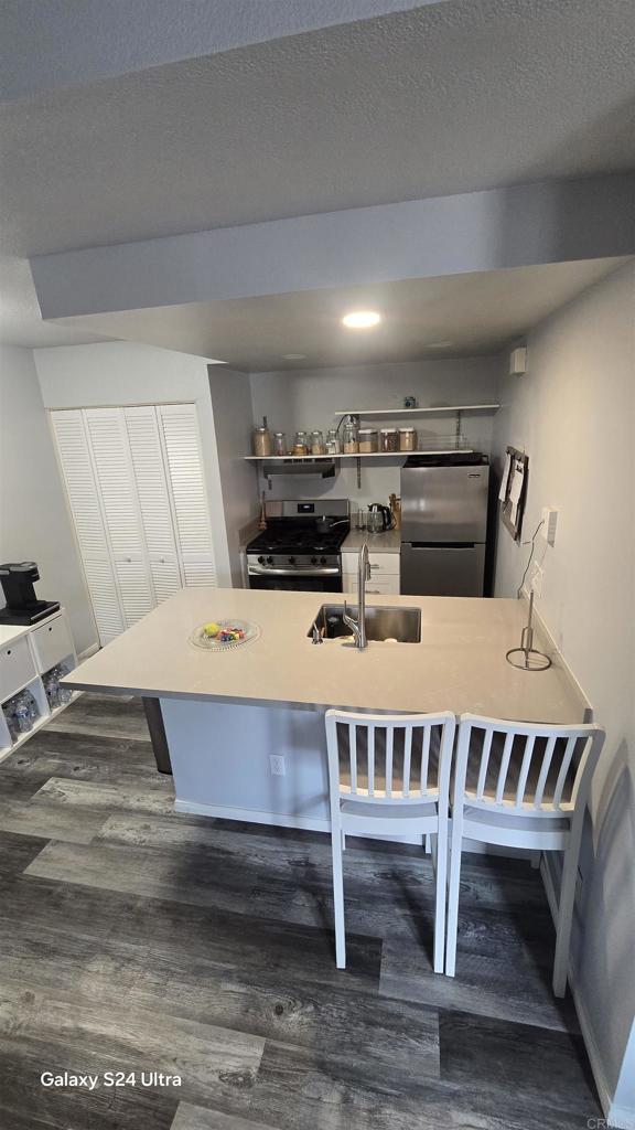 kitchen with a breakfast bar area, a sink, baseboards, dark wood-style floors, and stainless steel appliances