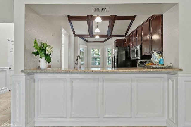 kitchen featuring dark brown cabinetry, light stone counters, stainless steel microwave, freestanding refrigerator, and coffered ceiling