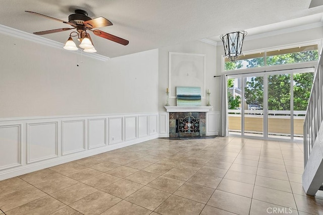 unfurnished living room featuring ceiling fan, a decorative wall, a fireplace, light tile patterned floors, and ornamental molding
