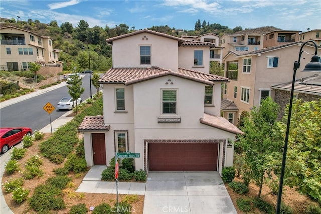 mediterranean / spanish-style home with a tile roof, a residential view, concrete driveway, an attached garage, and stucco siding