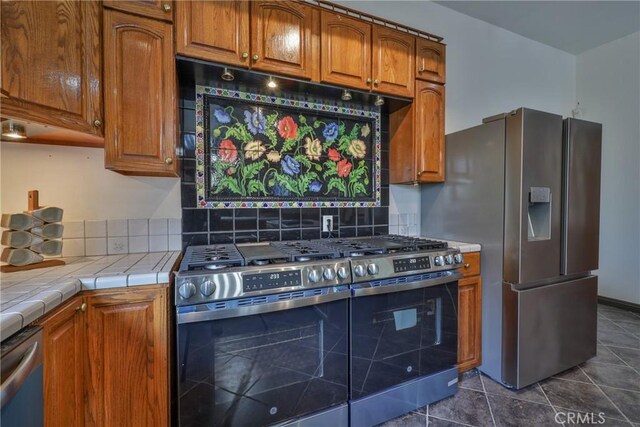kitchen featuring dark tile patterned flooring, brown cabinets, stainless steel appliances, and tile countertops