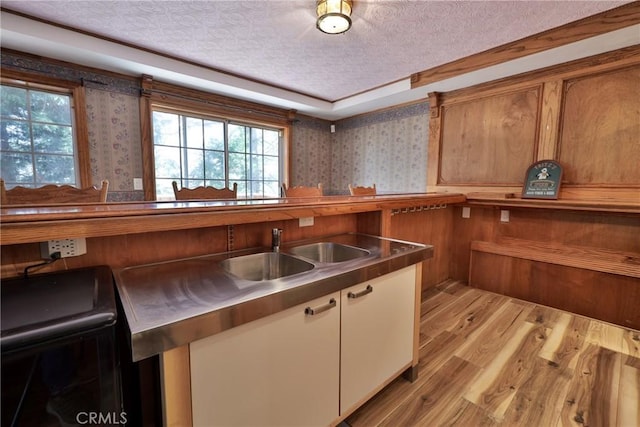 kitchen with light wood-style floors, a sink, a textured ceiling, and wallpapered walls