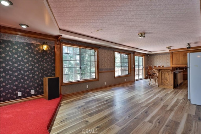 unfurnished living room with indoor bar, wallpapered walls, and wood finished floors