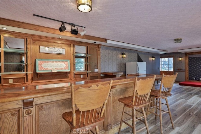 bar with freestanding refrigerator, wallpapered walls, and wood finished floors
