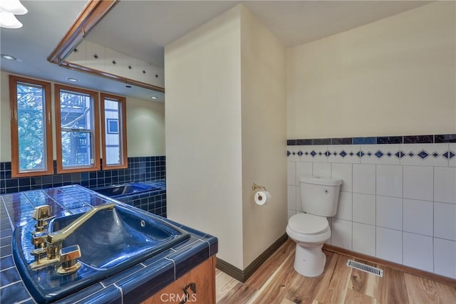 bathroom featuring visible vents, wood finished floors, toilet, tile walls, and recessed lighting