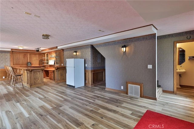 kitchen with light wood-style flooring, a wainscoted wall, freestanding refrigerator, wallpapered walls, and visible vents