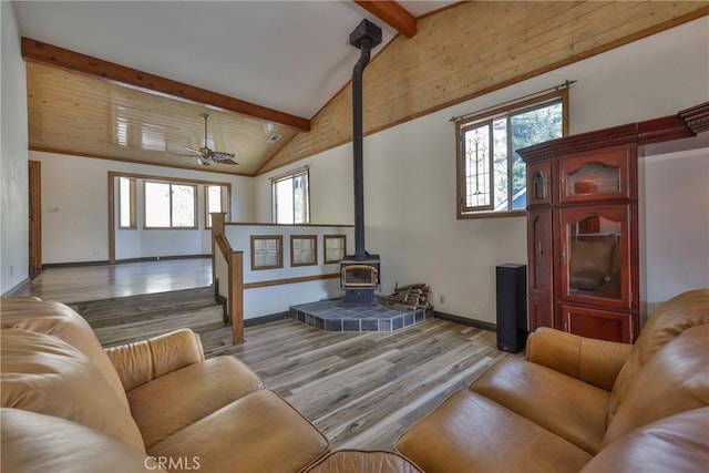 living room with a wood stove, baseboards, wood finished floors, beamed ceiling, and stairway