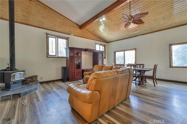 living room with a ceiling fan, a wood stove, wood finished floors, baseboards, and beamed ceiling