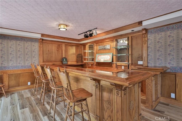 bar with wallpapered walls, wet bar, and light wood-style floors