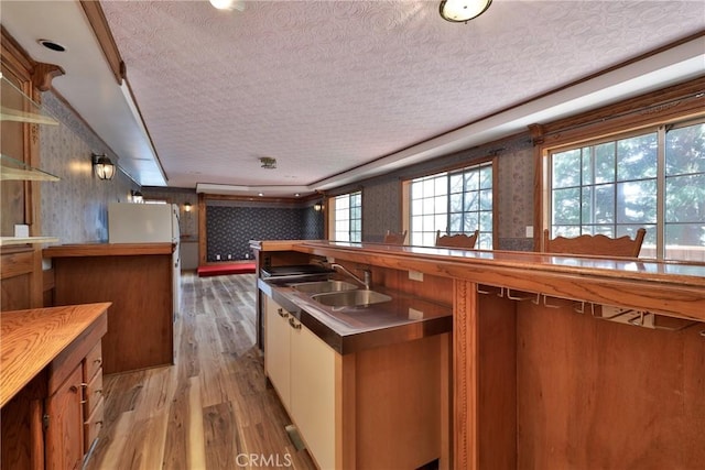 kitchen with brown cabinets, a sink, light wood-style floors, a textured ceiling, and wallpapered walls