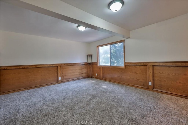 carpeted empty room with a wainscoted wall and beamed ceiling