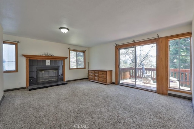 unfurnished living room with a tiled fireplace, baseboards, and carpet flooring