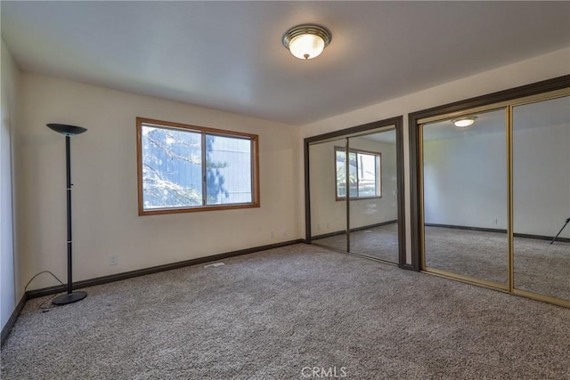 unfurnished bedroom featuring two closets, baseboards, and carpet