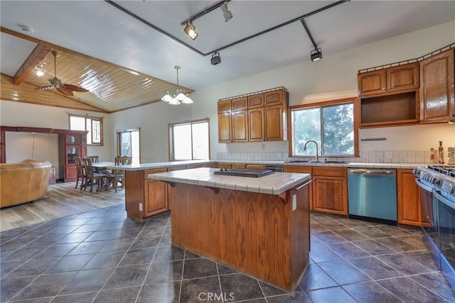 kitchen featuring brown cabinetry, tile countertops, a center island, stainless steel dishwasher, and a sink
