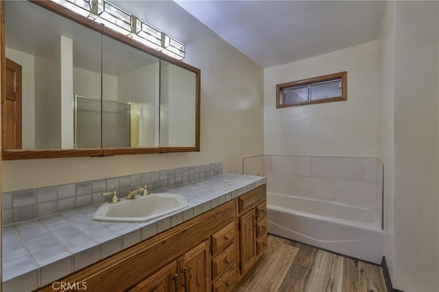 full bath with vanity, a bath, and wood finished floors