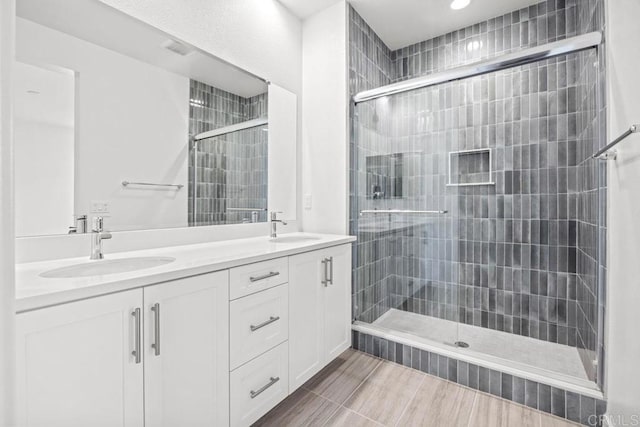 full bath featuring a sink, a tile shower, recessed lighting, and double vanity
