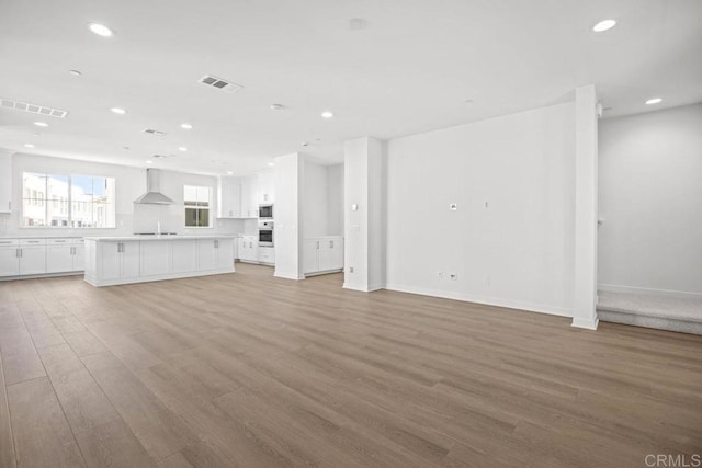 unfurnished living room with light wood-style floors, recessed lighting, a sink, and visible vents