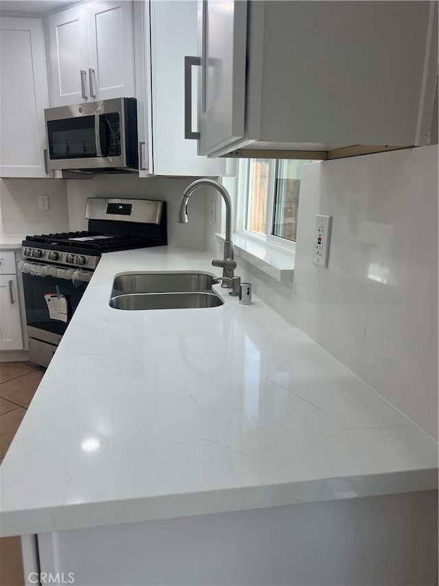 kitchen featuring a sink, appliances with stainless steel finishes, light tile patterned floors, and white cabinets