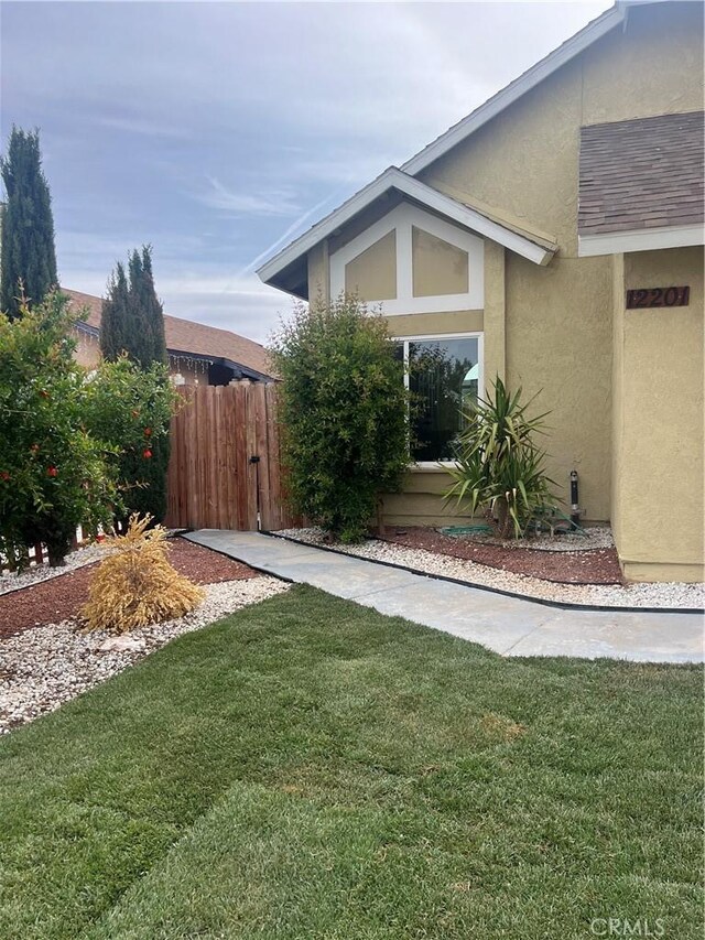 view of side of home with stucco siding, a yard, and fence
