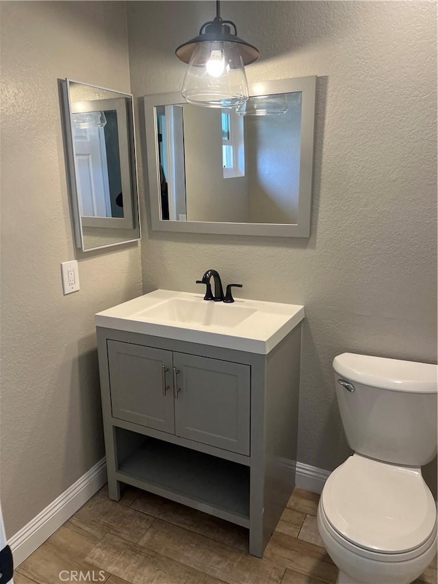 half bath with vanity, baseboards, a textured wall, and toilet