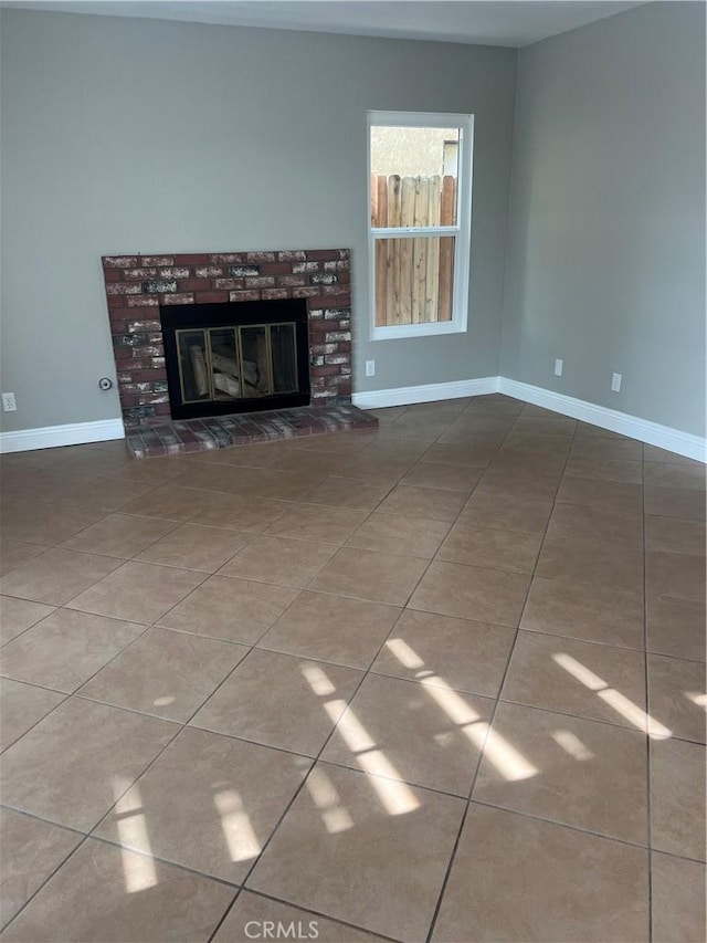 unfurnished living room featuring baseboards, a brick fireplace, and tile patterned floors