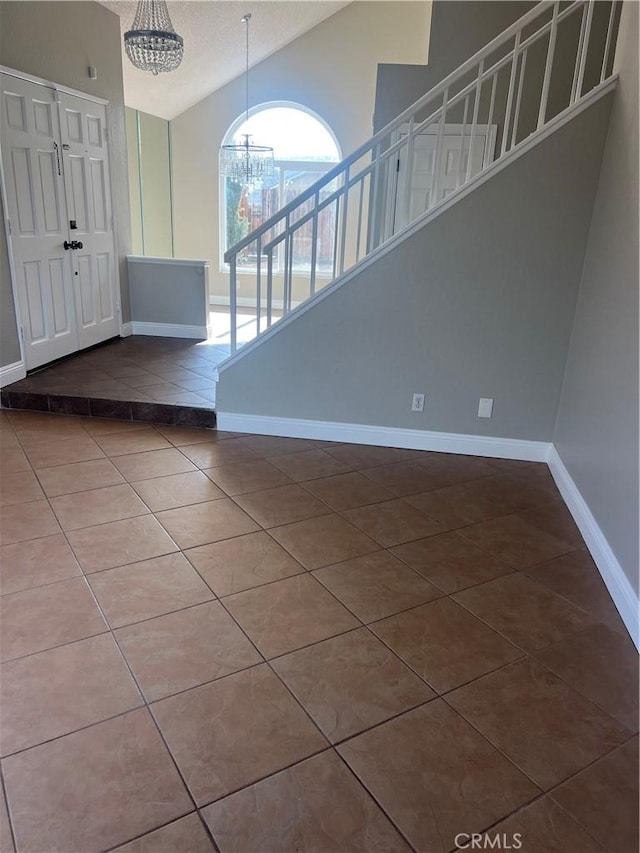 tiled foyer featuring stairway, baseboards, a notable chandelier, and vaulted ceiling