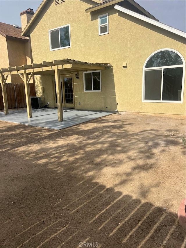 back of house featuring a chimney, a patio area, fence, a pergola, and stucco siding