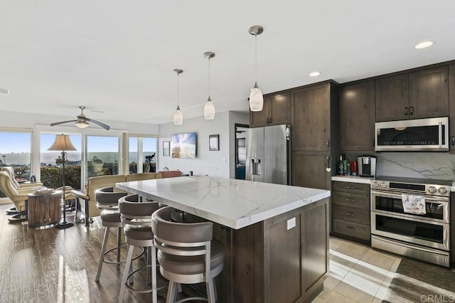 kitchen featuring dark brown cabinets, a center island, a ceiling fan, appliances with stainless steel finishes, and hanging light fixtures