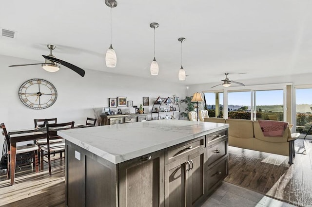 kitchen featuring ceiling fan, visible vents, decorative light fixtures, a center island, and light stone countertops