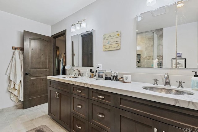 full bathroom with a sink, a tile shower, and double vanity