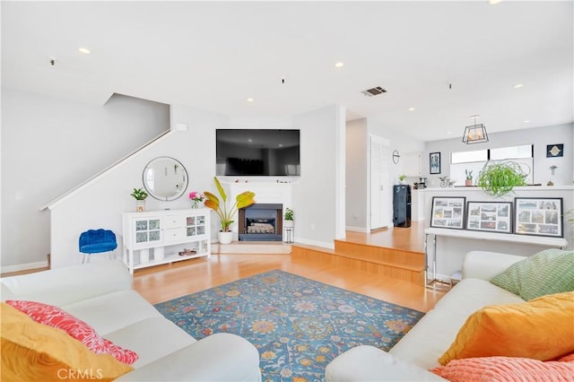 living room with visible vents, wood finished floors, baseboards, recessed lighting, and a fireplace with raised hearth