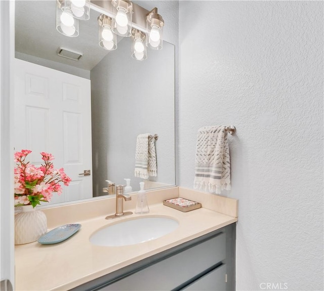 bathroom with a textured wall, visible vents, and vanity