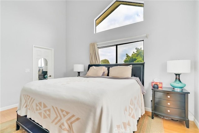 bedroom with baseboards, wood finished floors, and a towering ceiling