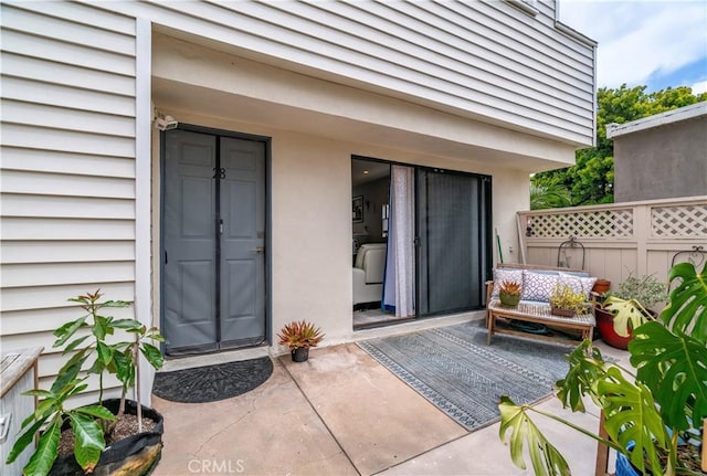 view of exterior entry featuring a patio, fence, and stucco siding