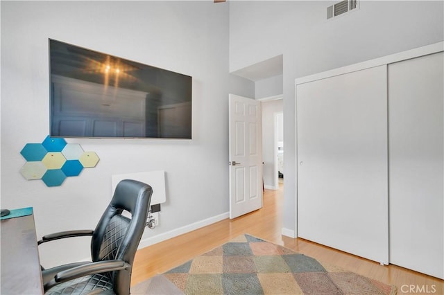 office space with visible vents, a high ceiling, baseboards, and wood finished floors
