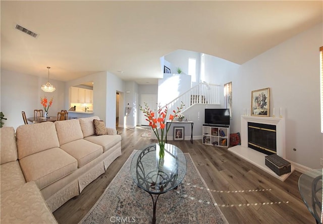 living area with baseboards, a glass covered fireplace, visible vents, stairs, and wood finished floors